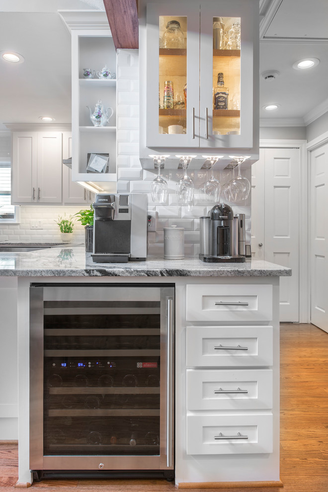 This is an example of a small transitional u-shaped wet bar in Other with an undermount sink, shaker cabinets, white cabinets, granite benchtops, white splashback, subway tile splashback, medium hardwood floors, brown floor and white benchtop.