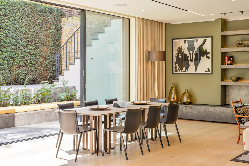 Contemporary open plan dining in London with green walls, light hardwood floors and beige floor.