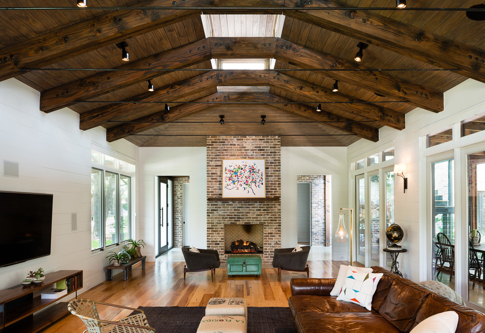 Photo of a country living room in Austin with white walls, medium hardwood floors, a standard fireplace, a brick fireplace surround and a wall-mounted tv.