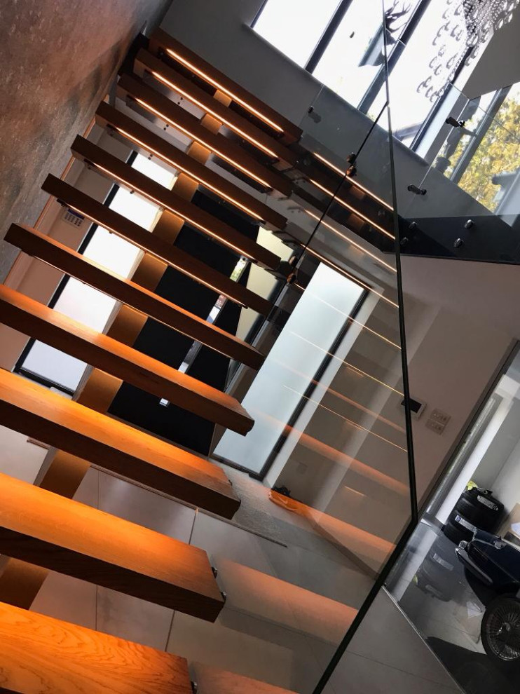 Идея дизайна: металлическая лестница на больцах, среднего размера в стиле модернизм с деревянными ступенями, стеклянными перилами и обоями на стенах