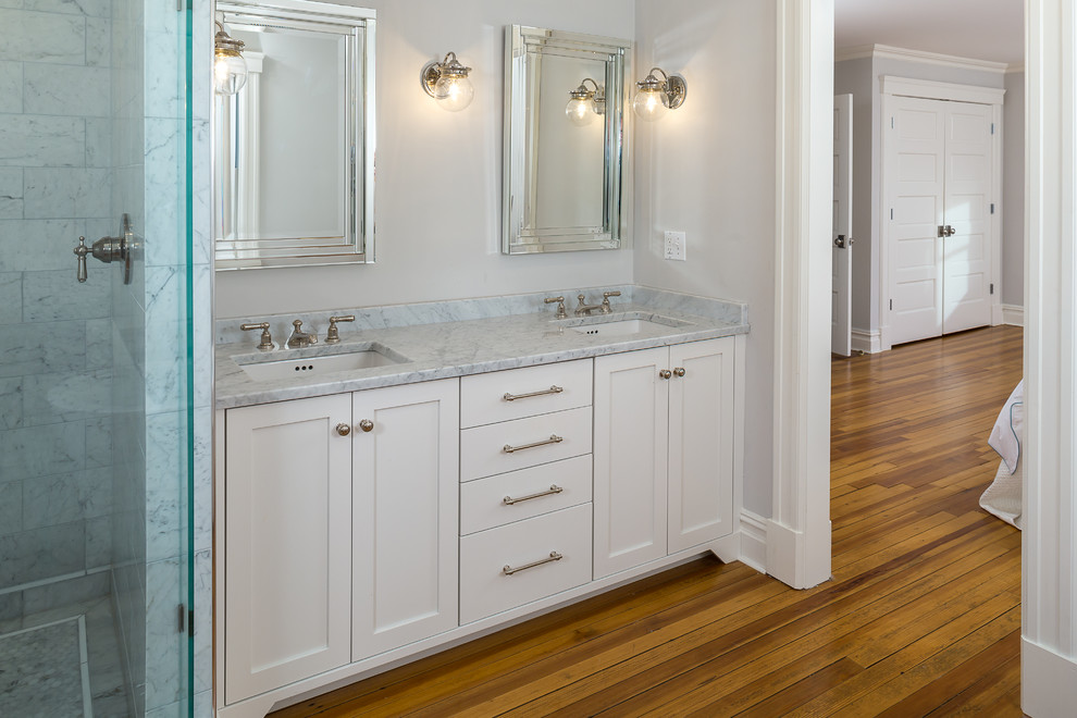 Inspiration for a large transitional master bathroom in New York with shaker cabinets, white cabinets, a freestanding tub, an alcove shower, gray tile, white tile, stone tile, an undermount sink, marble benchtops, grey walls, medium hardwood floors, brown floor and a hinged shower door.