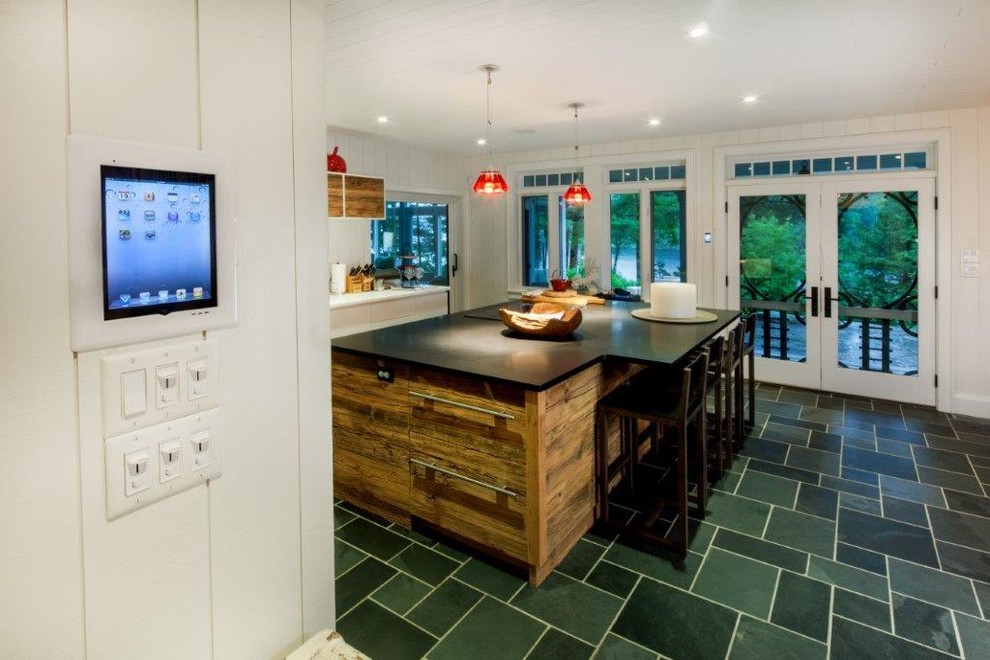 Mid-sized mountain style single-wall slate floor and green floor enclosed kitchen photo with a farmhouse sink, flat-panel cabinets, distressed cabinets, quartz countertops, white backsplash, wood backsplash, stainless steel appliances and an island