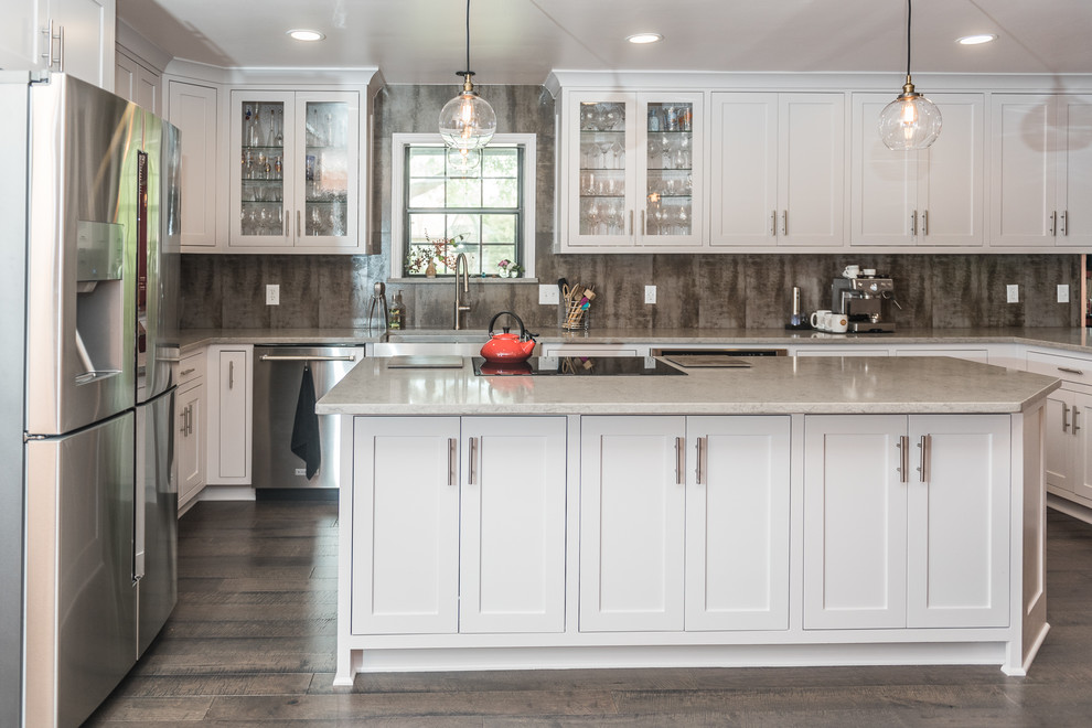 Large country kitchen in Dallas with a farmhouse sink, glass-front cabinets, white cabinets, quartz benchtops, grey splashback, porcelain splashback, stainless steel appliances, dark hardwood floors, with island and grey floor.