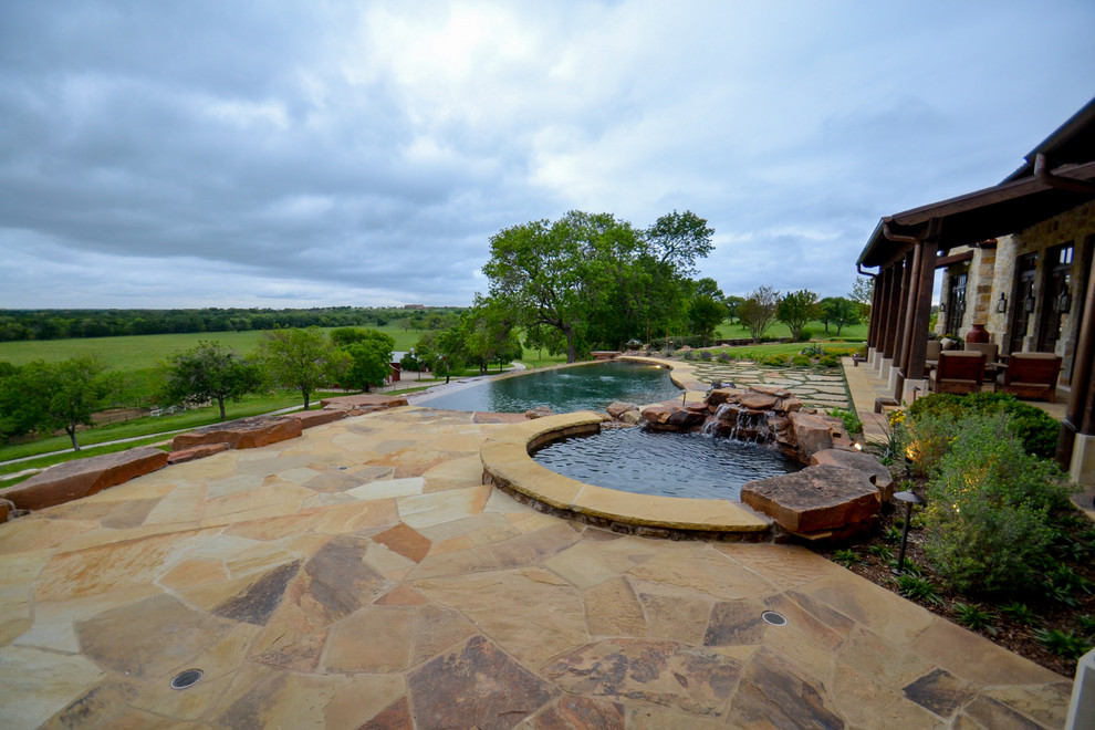 Design ideas for a mid-sized country backyard custom-shaped infinity pool in Dallas with a water feature and natural stone pavers.