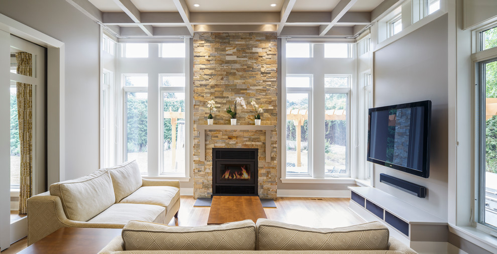 Small country enclosed family room in Ottawa with grey walls, medium hardwood floors, a standard fireplace, a stone fireplace surround and a wall-mounted tv.