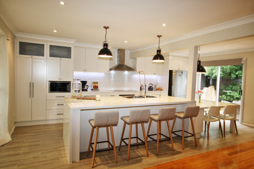 Design ideas for a large transitional single-wall kitchen in Sydney with a double-bowl sink, shaker cabinets, white cabinets, quartz benchtops, white splashback, subway tile splashback, stainless steel appliances, porcelain floors and with island.