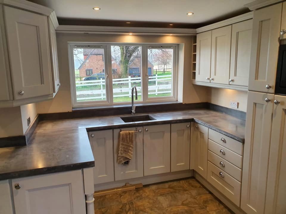 Photo of a country kitchen in Other with white cabinets, concrete benchtops, grey splashback, stone slab splashback, black appliances and grey benchtop.
