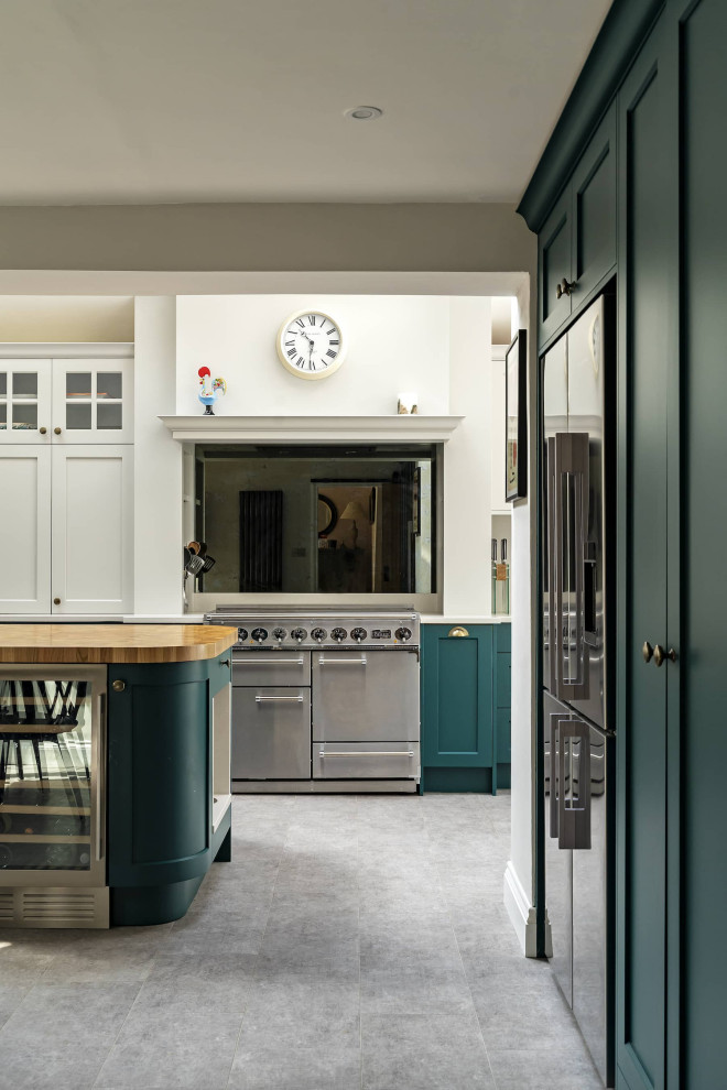 Inspiration for a large traditional u-shaped eat-in kitchen in Oxfordshire with a farmhouse sink, shaker cabinets, green cabinets, wood benchtops, white splashback, stainless steel appliances, ceramic floors, with island, grey floor, brown benchtop and exposed beam.