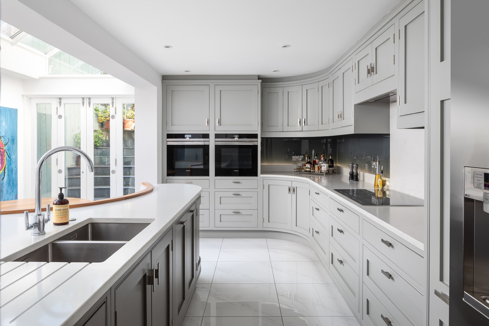 Inspiration for a transitional l-shaped kitchen in Other with a double-bowl sink, shaker cabinets, grey cabinets, grey splashback, glass sheet splashback, black appliances, with island, white floor and white benchtop.