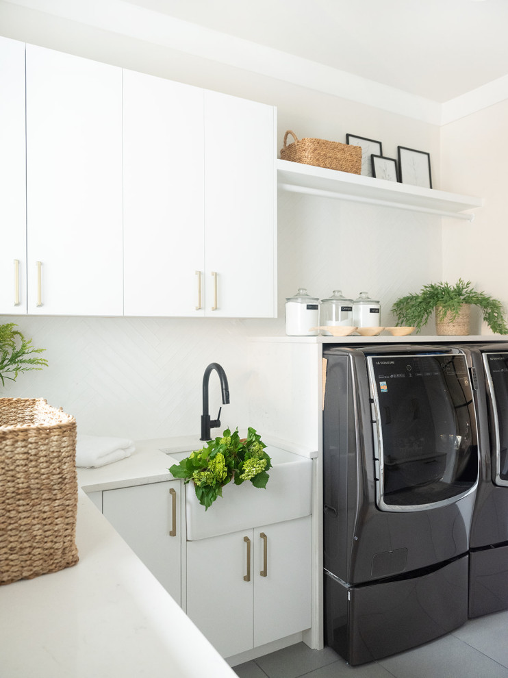 Design ideas for a contemporary l-shaped laundry room in Seattle with a farmhouse sink, flat-panel cabinets, white cabinets, white splashback, beige walls, grey floor and white benchtop.