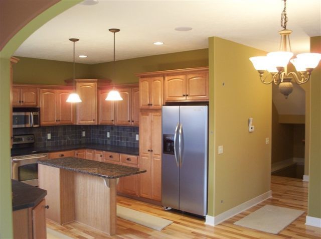 Mid-sized traditional u-shaped eat-in kitchen in Grand Rapids with flat-panel cabinets, light wood cabinets, granite benchtops, black splashback, stone tile splashback, stainless steel appliances, with island and light hardwood floors.