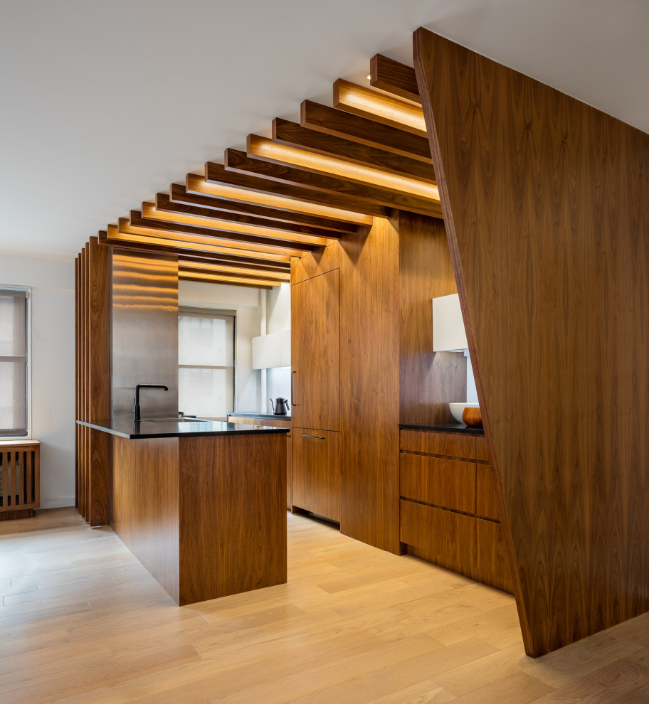 Inspiration for a galley medium tone wood floor and brown floor open concept kitchen remodel in New York with an undermount sink, flat-panel cabinets, medium tone wood cabinets, quartz countertops, white backsplash, glass sheet backsplash, paneled appliances, an island and black countertops