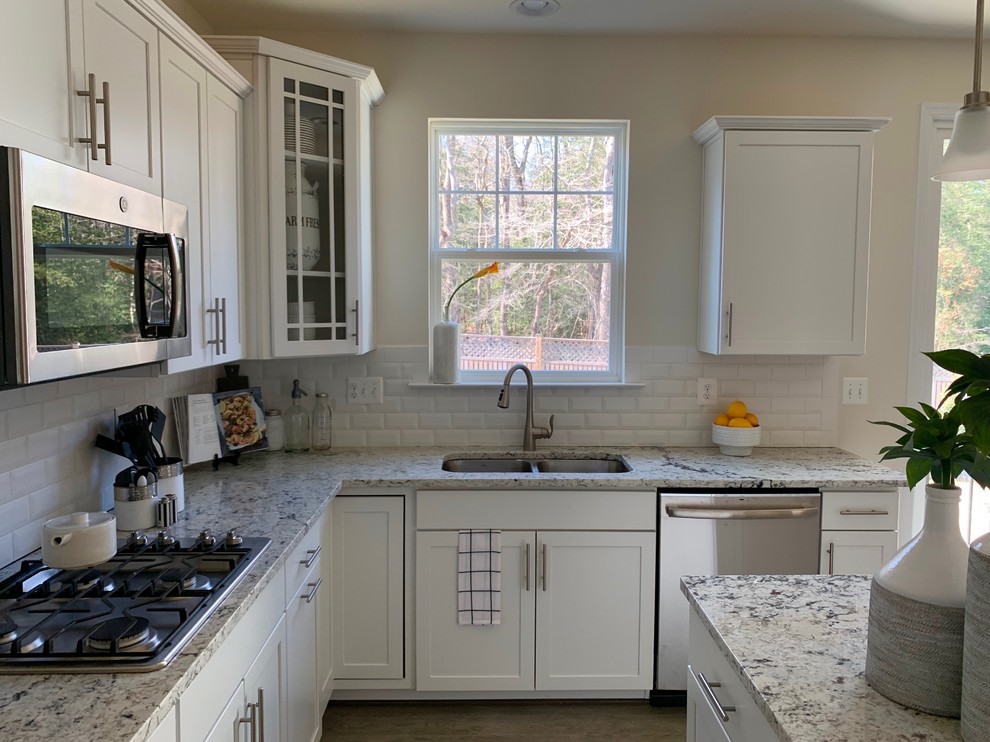 Photo of a mid-sized contemporary u-shaped eat-in kitchen in Baltimore with a double-bowl sink, shaker cabinets, white cabinets, granite benchtops, white splashback, subway tile splashback, stainless steel appliances, medium hardwood floors, with island, grey floor and grey benchtop.