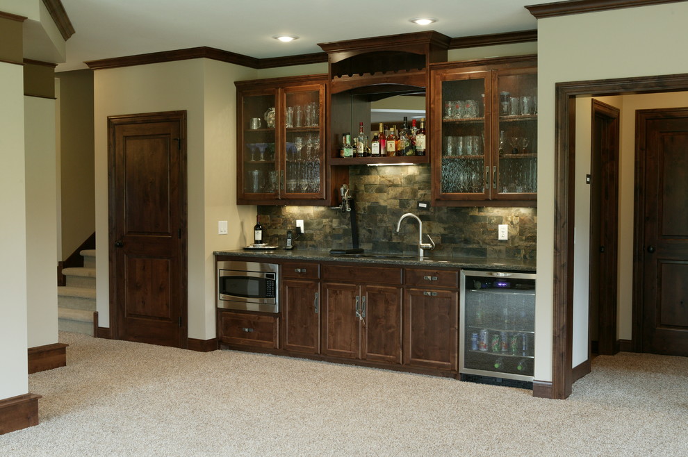 Small traditional single-wall wet bar in Minneapolis with an undermount sink, glass-front cabinets, dark wood cabinets, granite benchtops, grey splashback, stone tile splashback and carpet.