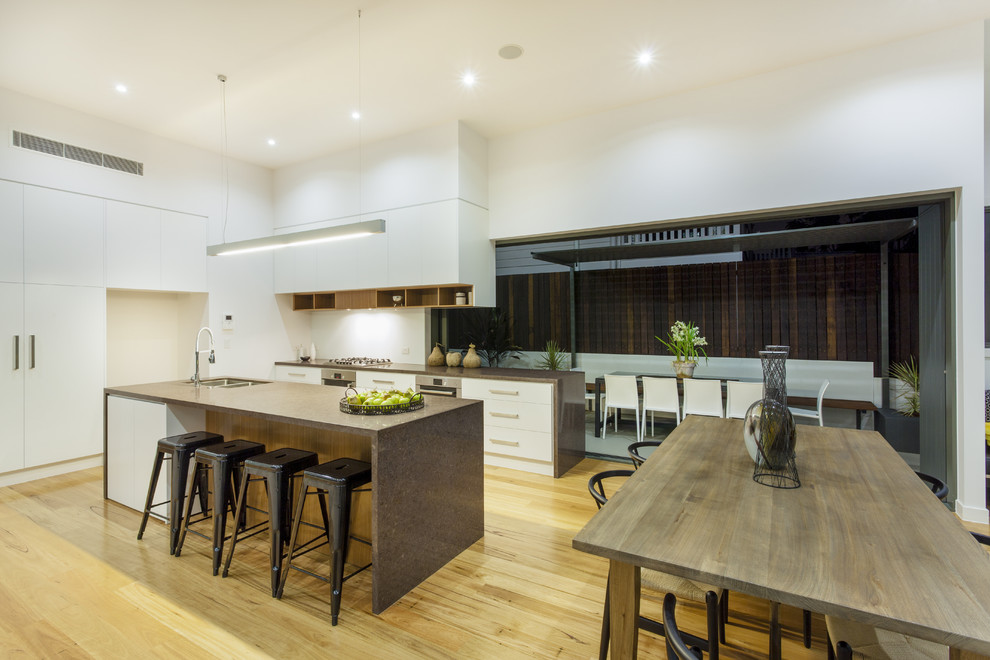 Mid-sized trendy single-wall medium tone wood floor and brown floor eat-in kitchen photo with a double-bowl sink, flat-panel cabinets, white cabinets, quartz countertops, paneled appliances and an island