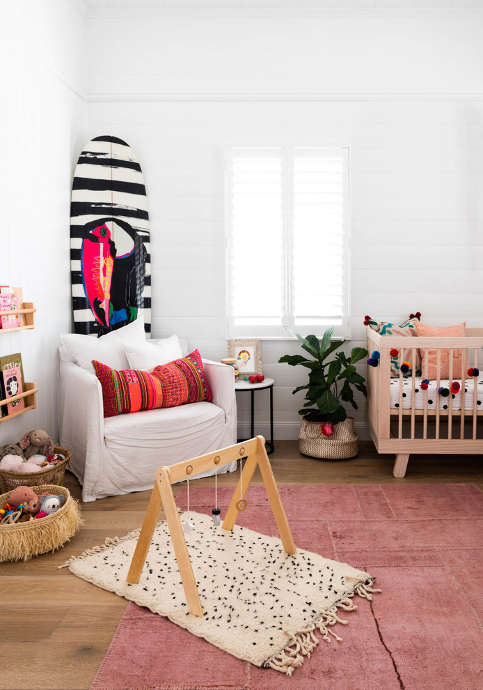 This is an example of a beach style nursery in Brisbane with white walls, medium hardwood floors and brown floor.