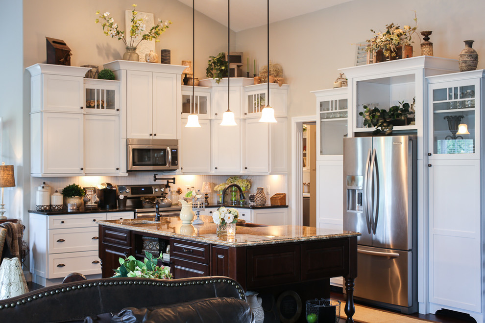 Example of a transitional l-shaped dark wood floor open concept kitchen design with a farmhouse sink, shaker cabinets, white cabinets, quartz countertops, white backsplash, stainless steel appliances and an island