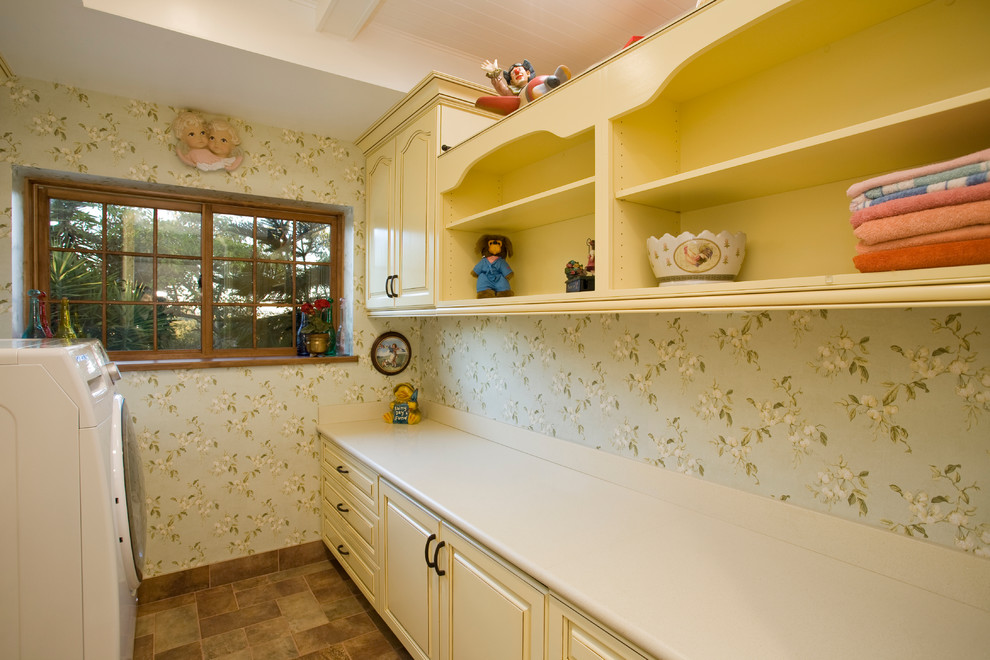 Mid-sized traditional galley dedicated laundry room in San Diego with an undermount sink, raised-panel cabinets, yellow cabinets, solid surface benchtops, green walls, porcelain floors and a side-by-side washer and dryer.