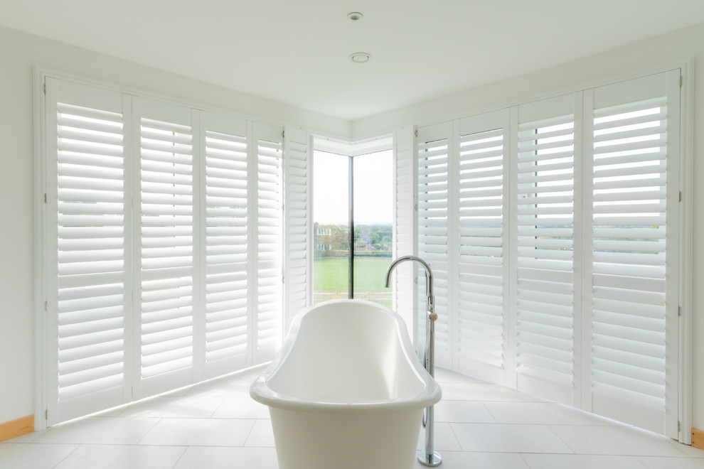 This is an example of a medium sized modern family bathroom in Sussex with freestanding cabinets, light wood cabinets, a freestanding bath, white tiles, white walls, ceramic flooring, a built-in sink, solid surface worktops, white floors and white worktops.