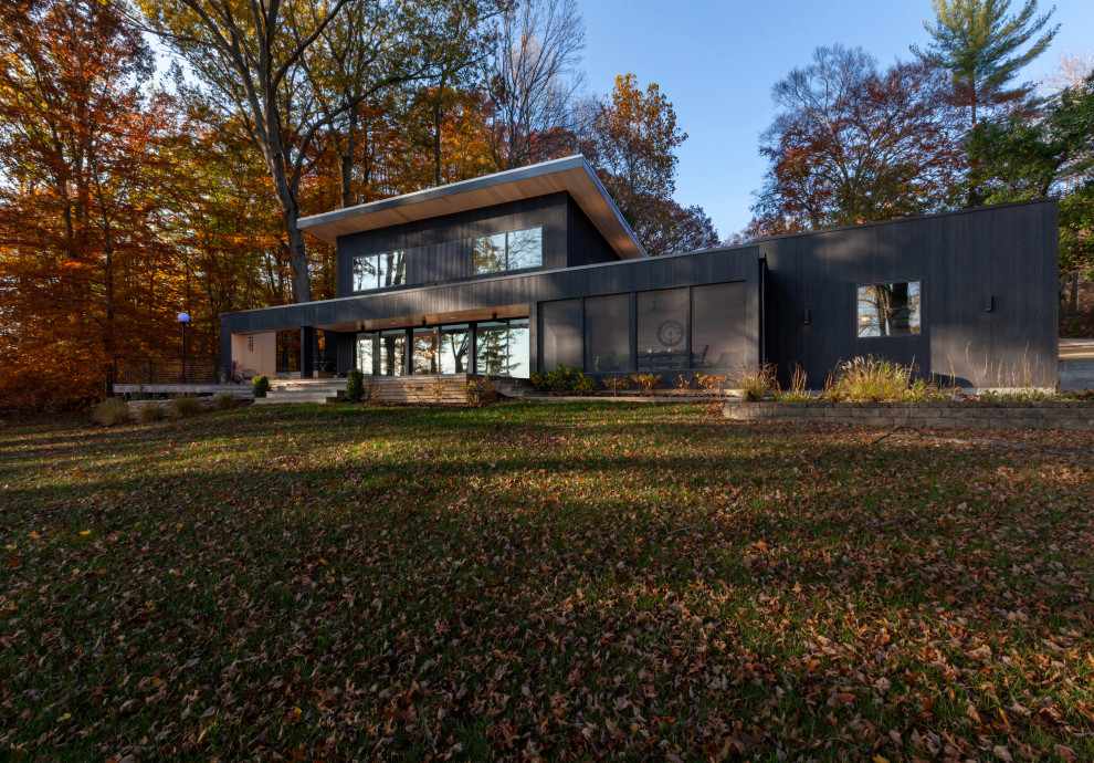 Idee per la facciata di una casa nera moderna a due piani di medie dimensioni con rivestimento in legno, copertura in metallo o lamiera, tetto grigio, pannelli e listelle di legno e terreno in pendenza