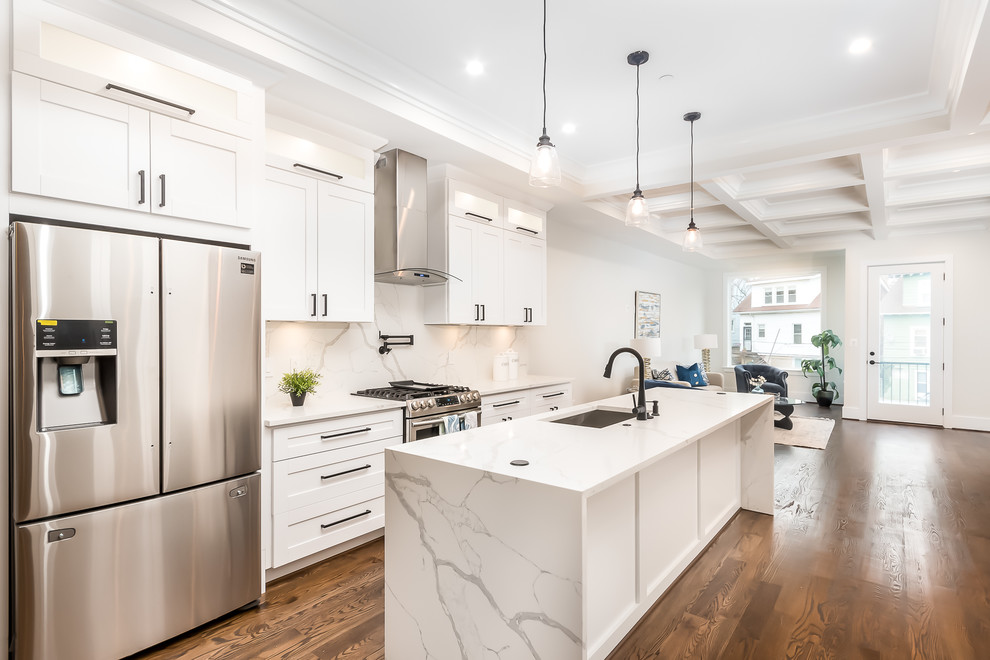 Transitional galley kitchen in DC Metro with an undermount sink, shaker cabinets, white cabinets, white splashback, stainless steel appliances, medium hardwood floors, with island, brown floor and white benchtop.