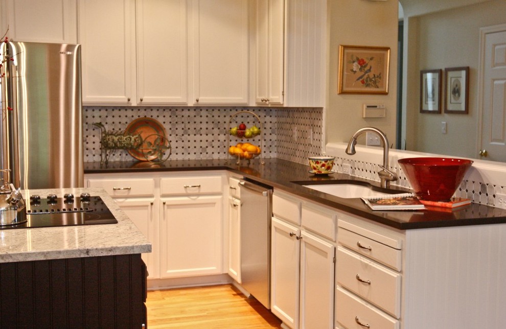 Mid-sized transitional u-shaped medium tone wood floor and brown floor open concept kitchen photo in Portland with an undermount sink, recessed-panel cabinets, white cabinets, quartz countertops, white backsplash, ceramic backsplash, stainless steel appliances, an island and black countertops