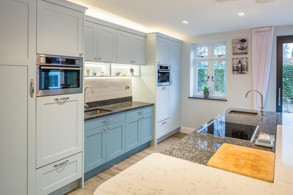 Design ideas for a large contemporary galley kitchen/diner with a built-in sink, shaker cabinets, turquoise cabinets, granite worktops, white splashback, stone tiled splashback, stainless steel appliances, medium hardwood flooring, multiple islands, brown floors and black worktops.