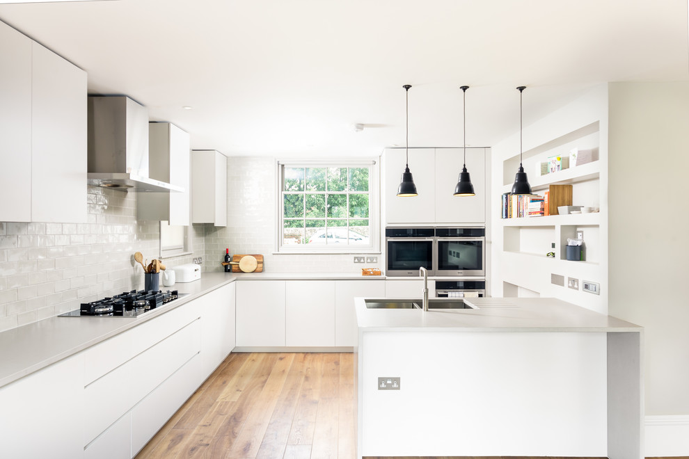 Inspiration for a mid-sized contemporary u-shaped kitchen in Sussex with flat-panel cabinets, a peninsula, grey benchtop, an undermount sink, white cabinets, white splashback, subway tile splashback, stainless steel appliances, medium hardwood floors and brown floor.