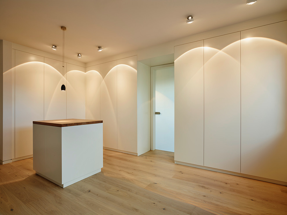 Large modern gender-neutral dressing room in Frankfurt with flat-panel cabinets, white cabinets, light hardwood floors and beige floor.