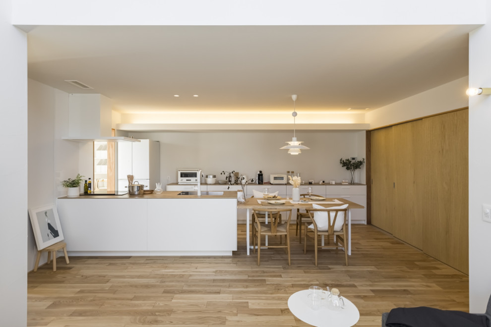 This is an example of a modern single-wall open plan kitchen in Other with an integrated sink, flat-panel cabinets, white cabinets, wood benchtops, white splashback, slate splashback, white appliances, light hardwood floors, with island, beige floor and brown benchtop.