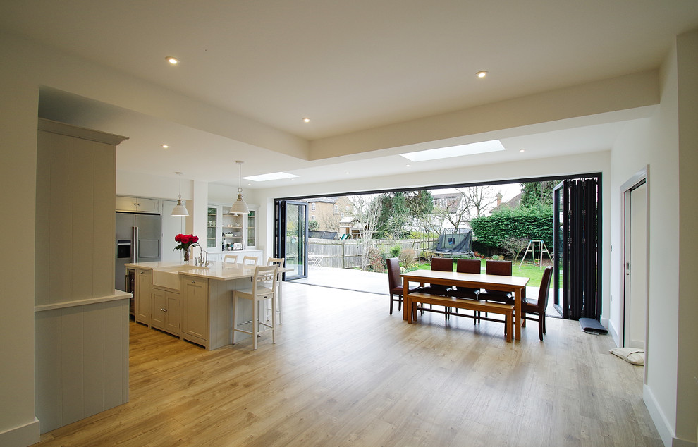 Mid-sized contemporary l-shaped eat-in kitchen with a farmhouse sink, shaker cabinets, grey cabinets, solid surface benchtops, white splashback, ceramic splashback, stainless steel appliances, vinyl floors and with island.