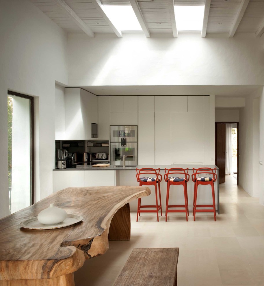 Inspiration for a mid-sized mediterranean u-shaped eat-in kitchen in London with flat-panel cabinets, white cabinets, stainless steel appliances, a peninsula and ceramic floors.