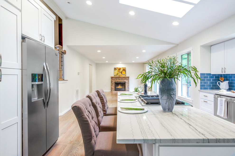 Example of a large transitional galley medium tone wood floor and brown floor open concept kitchen design in Orange County with shaker cabinets, white cabinets, quartz countertops, blue backsplash, subway tile backsplash, stainless steel appliances, an island, multicolored countertops and an undermount sink