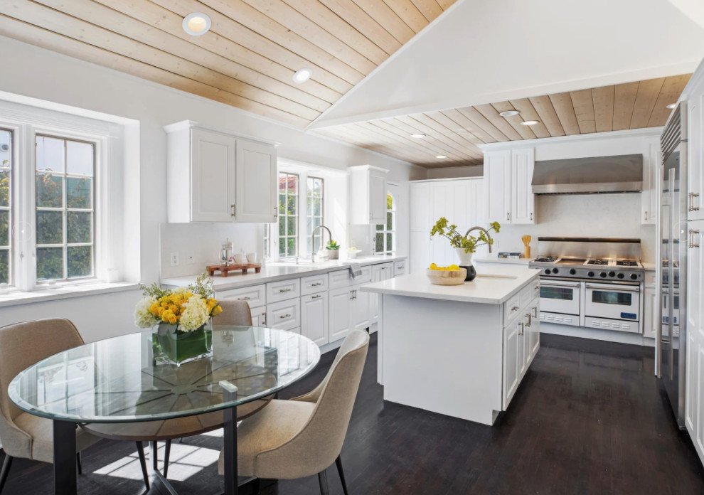 Bild på ett avskilt, stort vit vitt u-kök, med en undermonterad diskho, luckor med upphöjd panel, vita skåp, bänkskiva i kvarts, vitt stänkskydd, stänkskydd i keramik, rostfria vitvaror, mörkt trägolv, en köksö och brunt golv