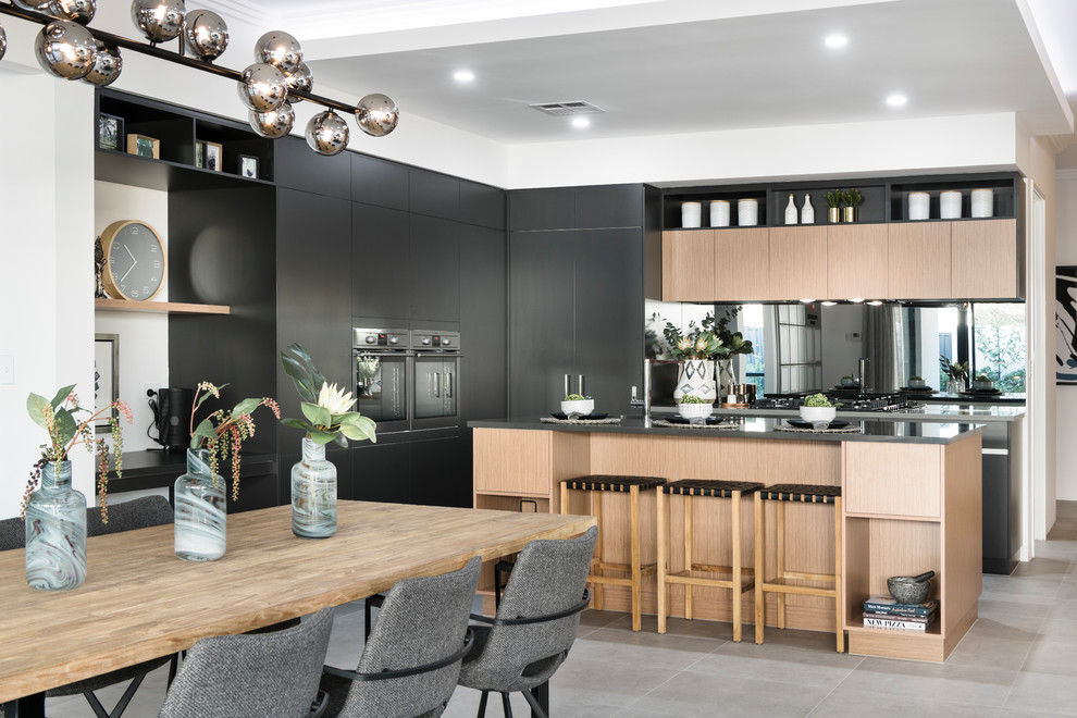 Mid-sized contemporary galley open plan kitchen in Perth with an undermount sink, flat-panel cabinets, black cabinets, solid surface benchtops, metallic splashback, mirror splashback, stainless steel appliances, ceramic floors, with island, grey floor and grey benchtop.