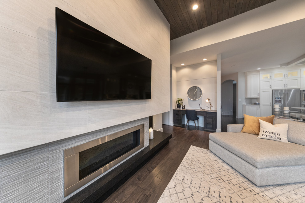 Design ideas for a large contemporary open concept living room in Edmonton with grey walls, dark hardwood floors, a standard fireplace, a tile fireplace surround, a wall-mounted tv, brown floor, timber and panelled walls.