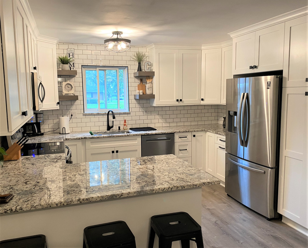 Photo of a mid-sized transitional u-shaped eat-in kitchen in Detroit with an undermount sink, shaker cabinets, white cabinets, granite benchtops, white splashback, subway tile splashback, stainless steel appliances, medium hardwood floors, a peninsula, grey floor and grey benchtop.