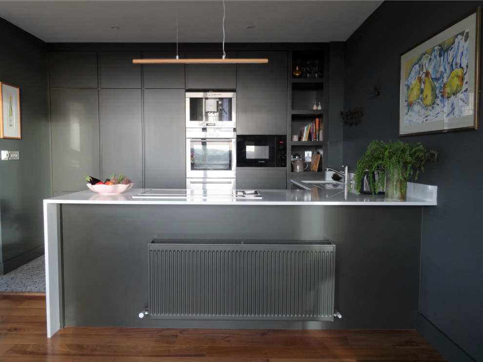 This is an example of a small contemporary u-shaped open plan kitchen in Dublin with flat-panel cabinets, quartzite benchtops, stainless steel appliances, terrazzo floors, multi-coloured floor and white benchtop.