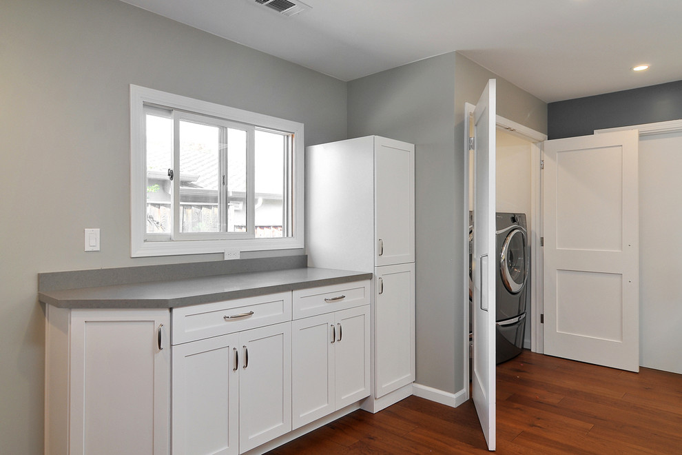 Design ideas for a mid-sized transitional single-wall laundry cupboard in San Francisco with shaker cabinets, white cabinets, grey walls, medium hardwood floors and a side-by-side washer and dryer.