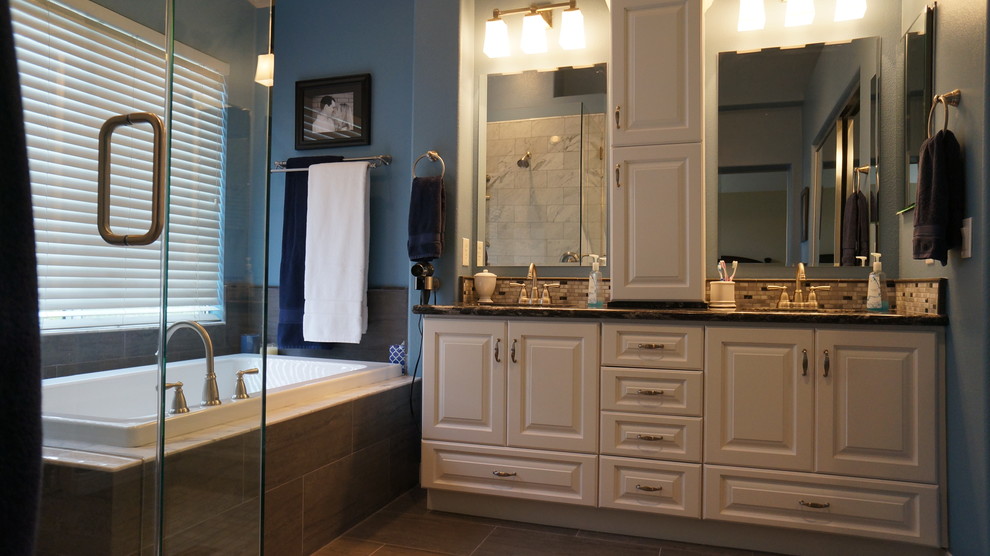 This is an example of a large transitional master bathroom in Orange County with raised-panel cabinets, white cabinets, a drop-in tub, an alcove shower, brown tile, blue walls, an undermount sink, brown floor and a hinged shower door.