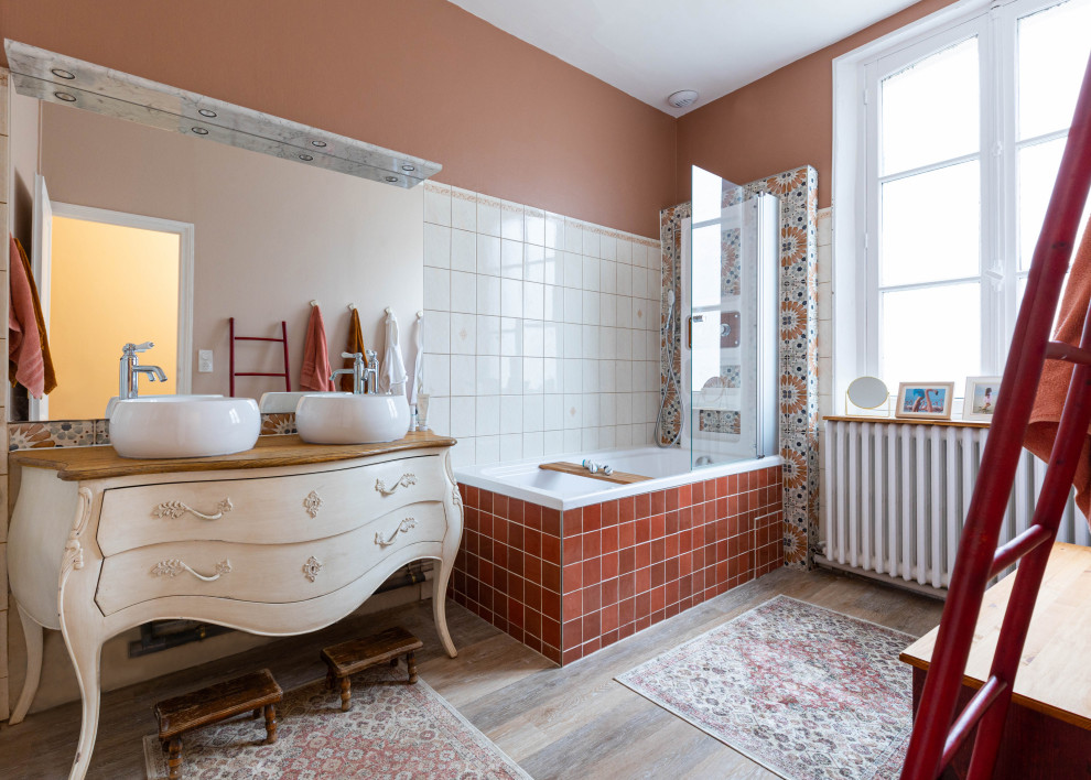 Design ideas for a mid-sized eclectic master bathroom in Paris with beige cabinets, an undermount tub, a shower/bathtub combo, a wall-mount toilet, white tile, orange tile, red tile, ceramic tile, pink walls, dark hardwood floors, a vessel sink, wood benchtops, brown floor, a hinged shower door, brown benchtops, a double vanity, a freestanding vanity and flat-panel cabinets.