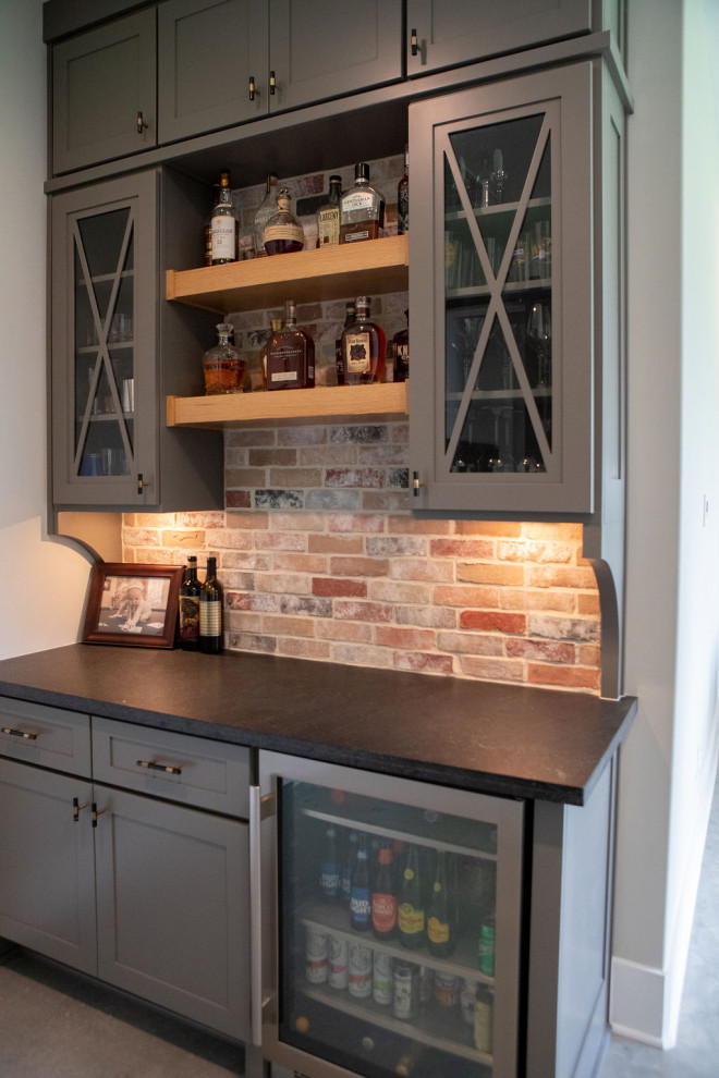 Photo of a small rural single-wall home bar in Houston with recessed-panel cabinets, grey cabinets, multi-coloured splashback, brick splashback, concrete flooring, grey floors and brown worktops.