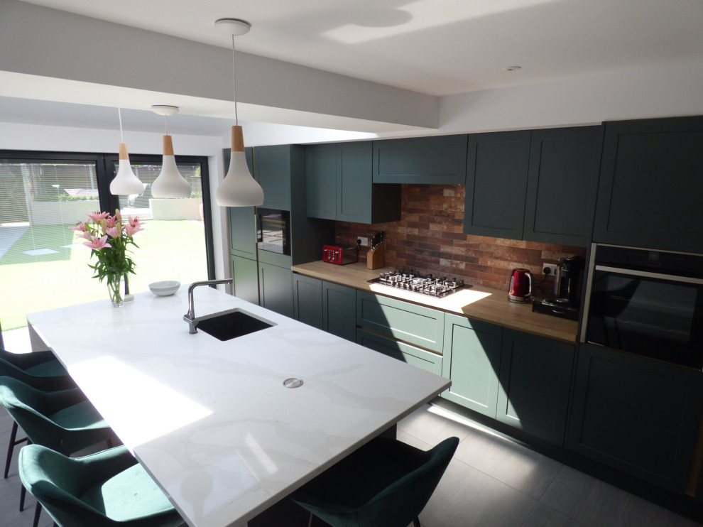 Design ideas for a mid-sized modern single-wall open plan kitchen in Other with an integrated sink, shaker cabinets, green cabinets, quartzite benchtops, brick splashback, panelled appliances, with island and white benchtop.