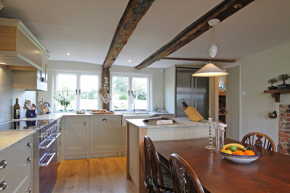 Design ideas for a large country l-shaped eat-in kitchen in Hampshire with shaker cabinets, beige cabinets, granite benchtops, a farmhouse sink, white splashback, stone slab splashback, dark hardwood floors, with island and stainless steel appliances.