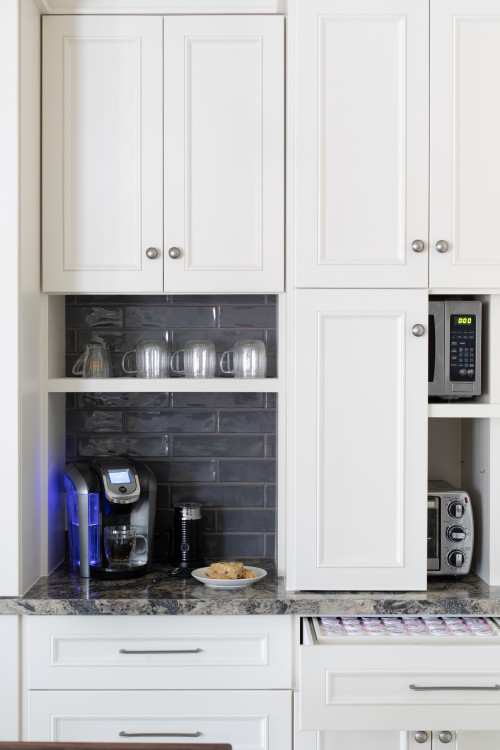 Compact coffee bar with white RTA cabinets, gray subway tile backsplash, granite countertop, and built-in shelves holding mugs beside a microwave and toaster.