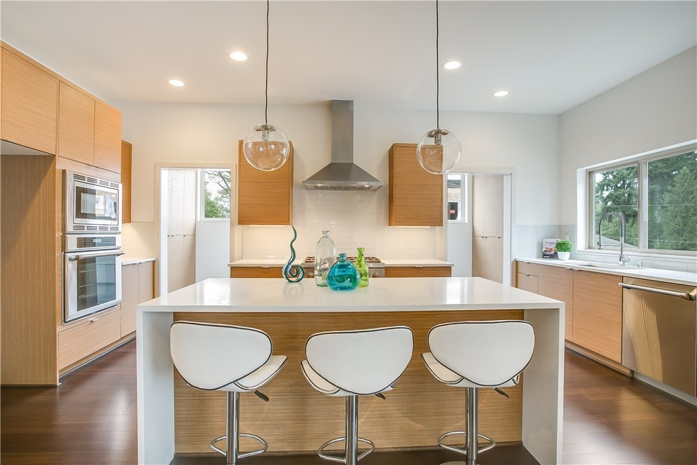 Photo of a modern l-shaped open plan kitchen in Seattle with flat-panel cabinets, stainless steel appliances, with island and white splashback.
