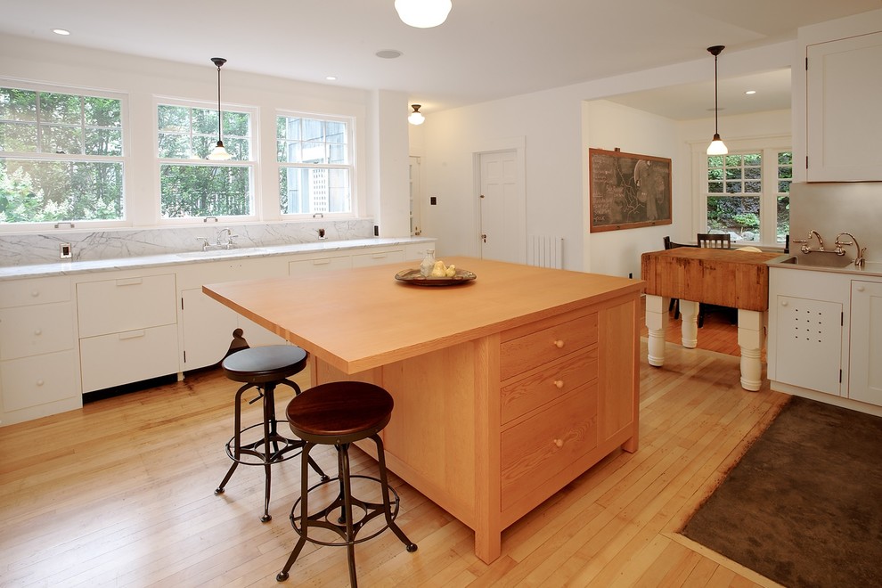 This is an example of a transitional eat-in kitchen in Seattle with flat-panel cabinets, white cabinets, white splashback, light hardwood floors and multiple islands.