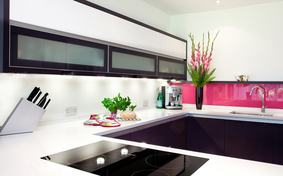 Design ideas for a mid-sized contemporary u-shaped open plan kitchen in London with an undermount sink, glass-front cabinets, black cabinets, solid surface benchtops, pink splashback, glass sheet splashback, black appliances and a peninsula.