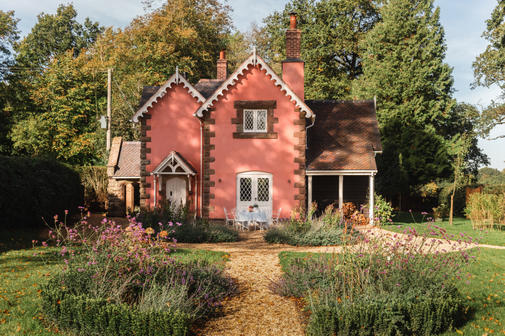 Стильный дизайн: маленький, двухэтажный, розовый частный загородный дом в викторианском стиле с двускатной крышей, черепичной крышей и коричневой крышей для на участке и в саду - последний тренд