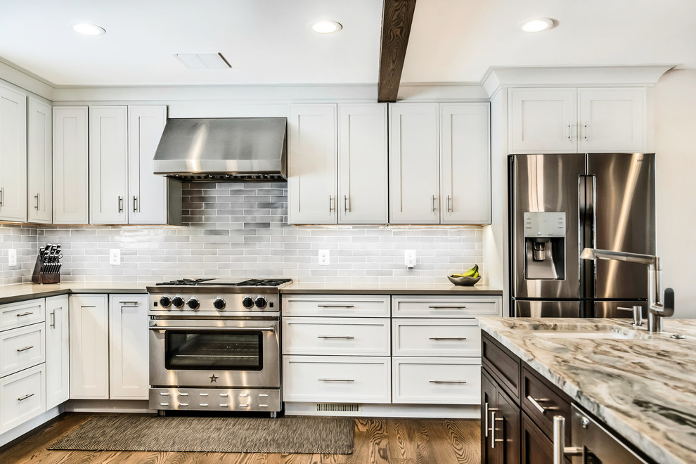 Transitional medium tone wood floor and brown floor eat-in kitchen photo in DC Metro with a farmhouse sink, shaker cabinets, white cabinets, granite countertops, white backsplash, subway tile backsplash, stainless steel appliances, an island and multicolored countertops